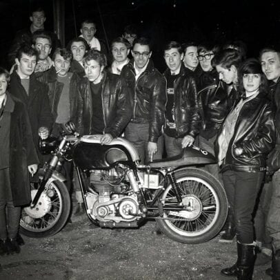 British teens stand around a cafe racer motorcycle circa 1960