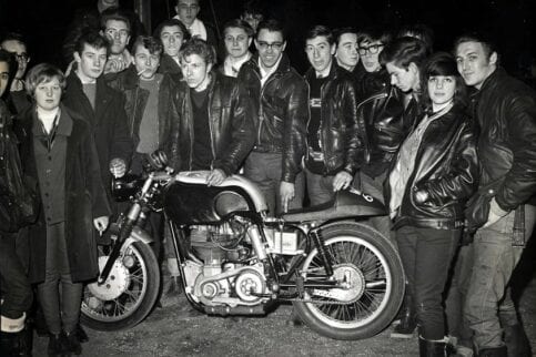 British teens stand around a cafe racer motorcycle circa 1960