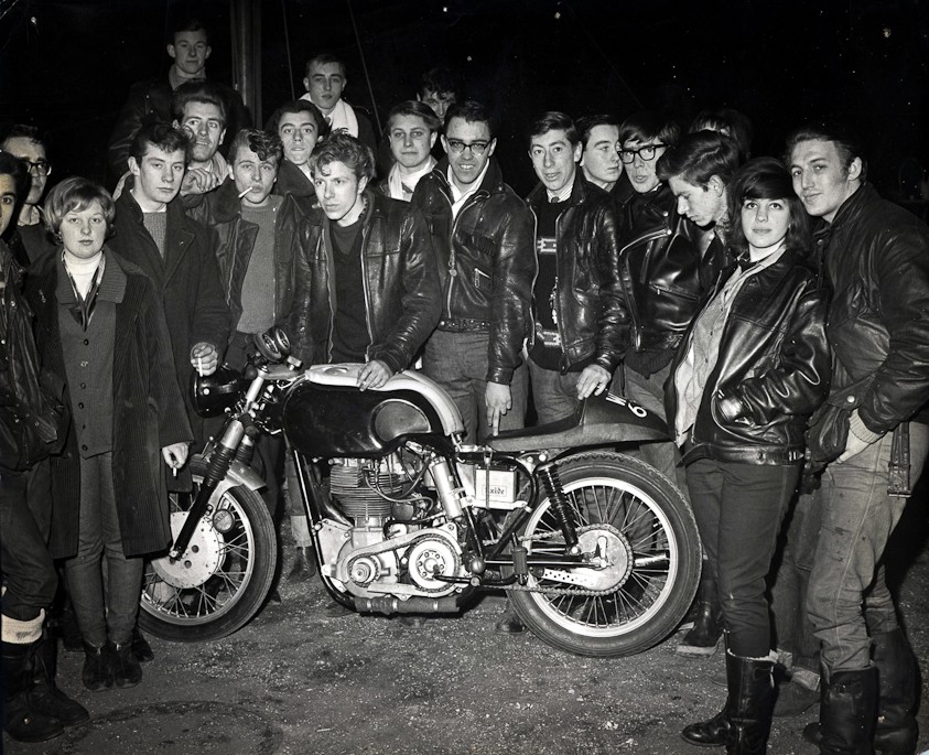 British teens stand around a cafe racer motorcycle circa 1960