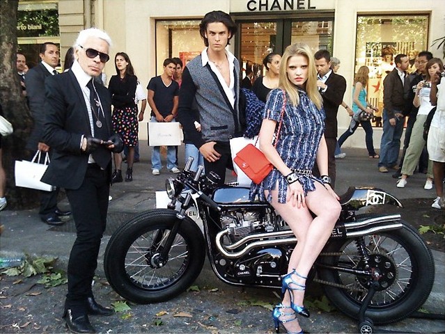 Karl Lagerfeld and two models pose for a photo while standing around a Chanel cafe racer