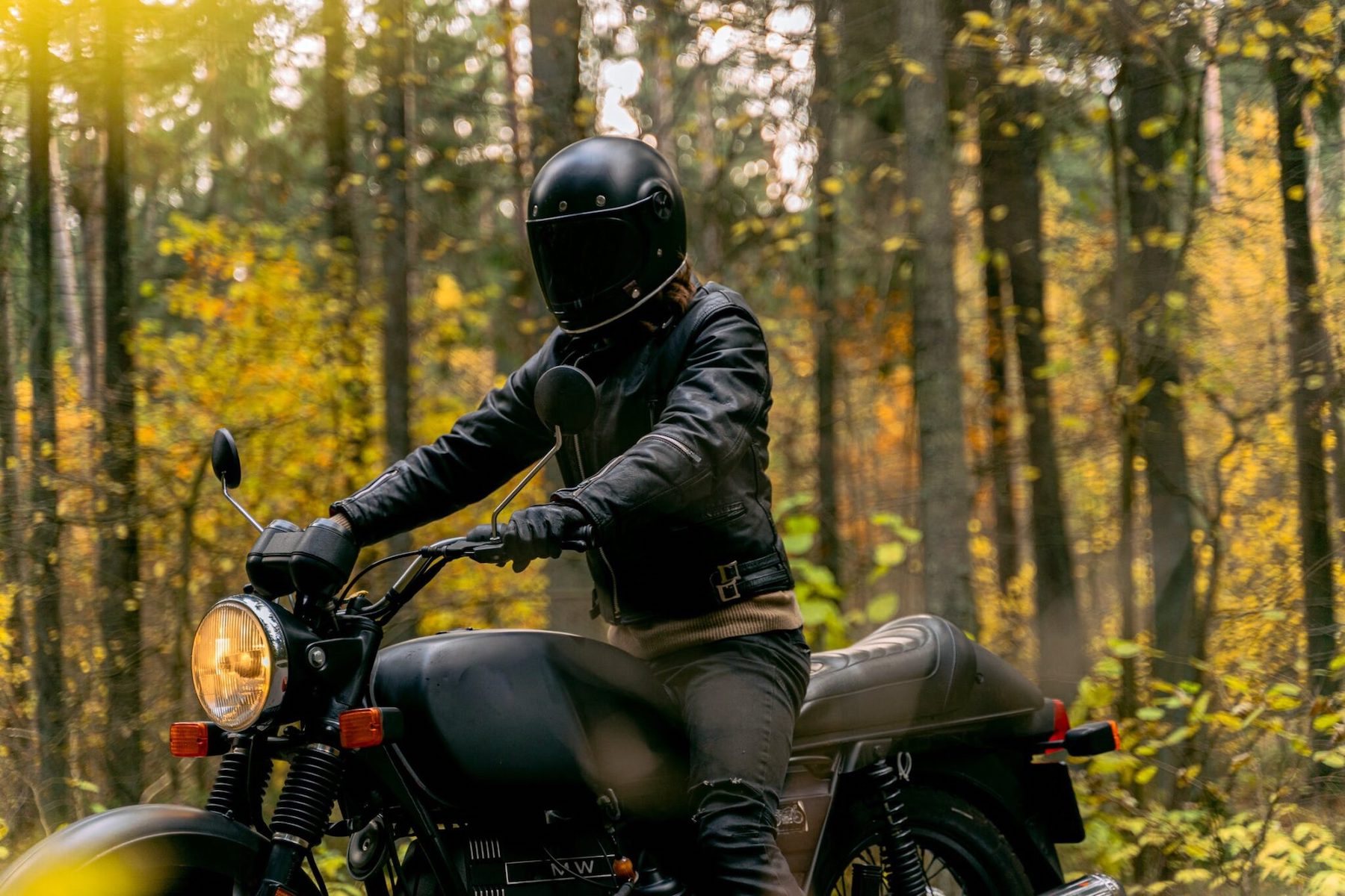 a motorcycle rider dressed in all-black look at the camera in a European forest