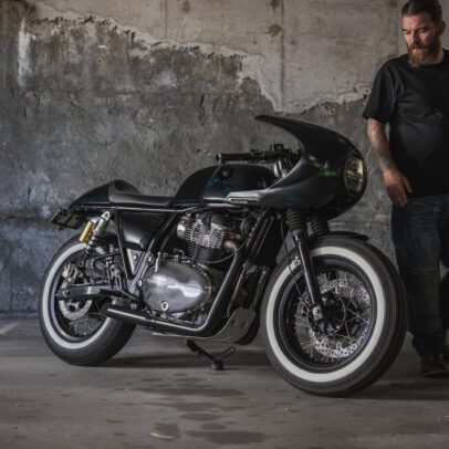 A side view of a Royal Enfield Continental GT 650 cafe racer with a man in a car park