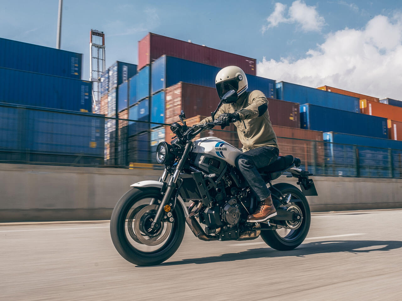 A 2020 Yamaha XSR700 motorcycle rides along a cargo container terminal