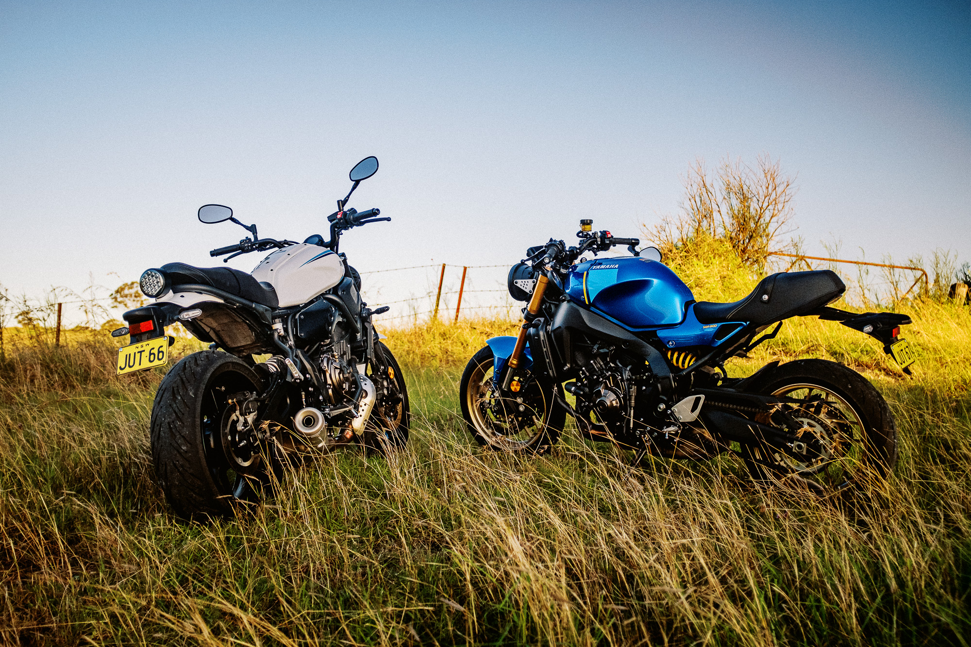 A 2020 Yamaha XSR700 motorcycle and a new XSR900 motorcycle stand on a hill at sunset in Sydney's outer rural suburbs