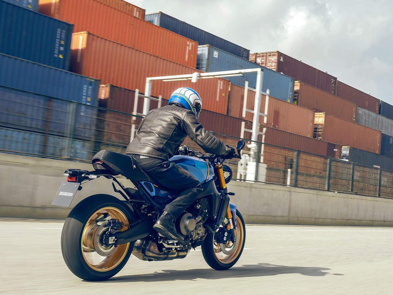 The 2022 Yamaha XSR900 motorcycle rides past a cargo container storage area