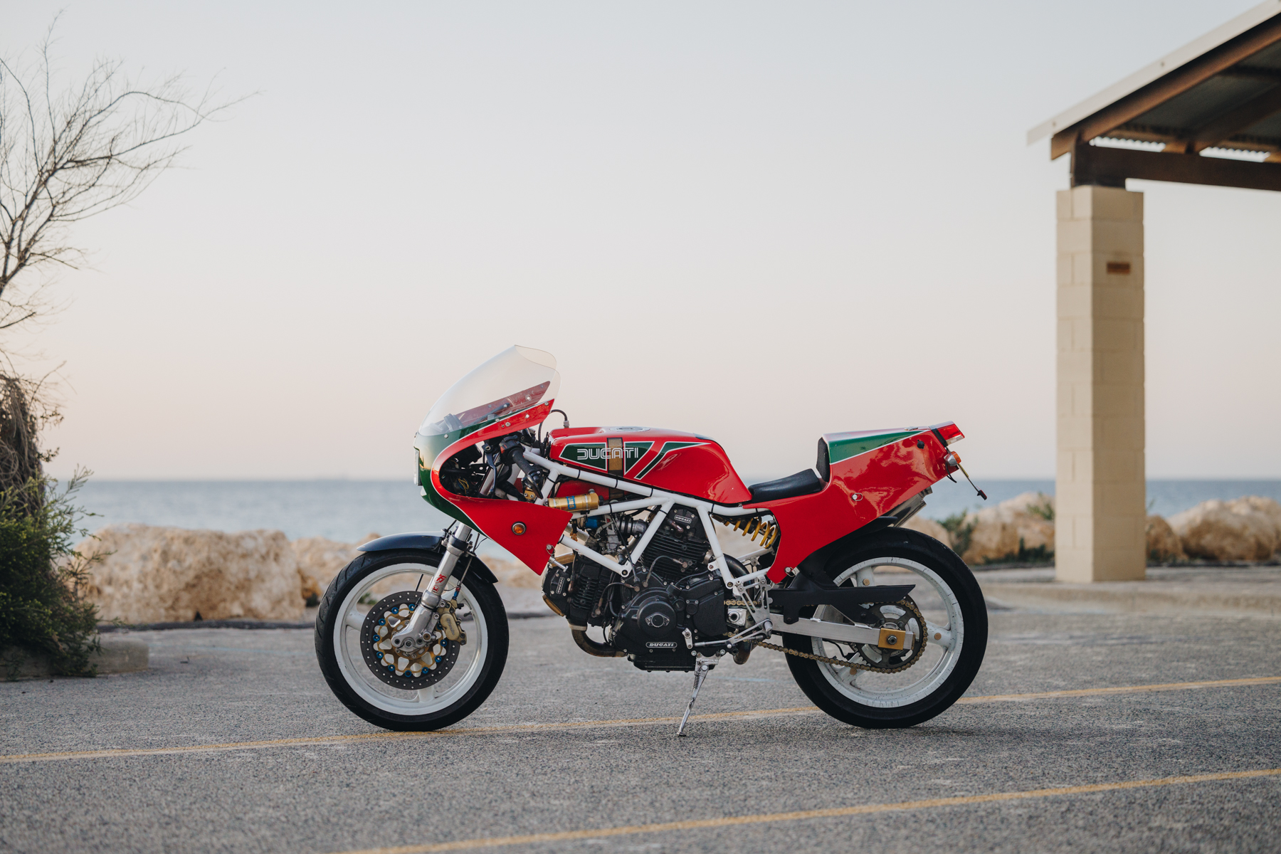 Side profile photo of a custom Ducati motorcycle parked at the beach